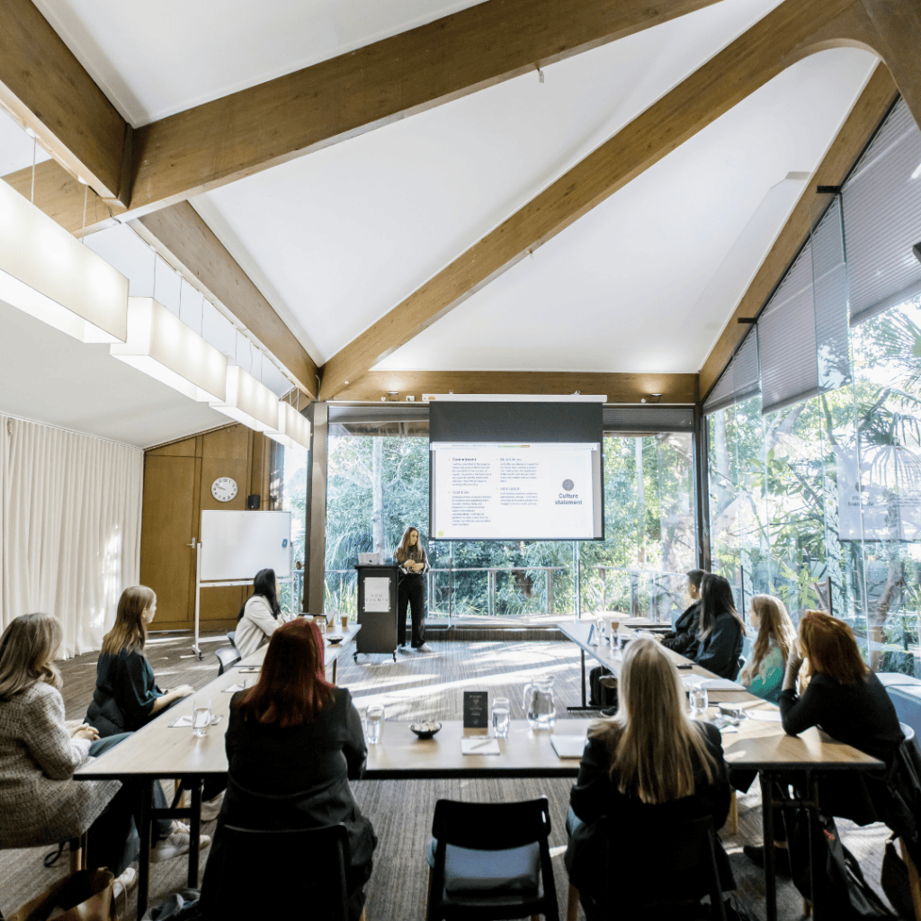 Conference setup in Melbourne Zoo's Rainforest Room with presenter, natural light and rainforest backdrop.